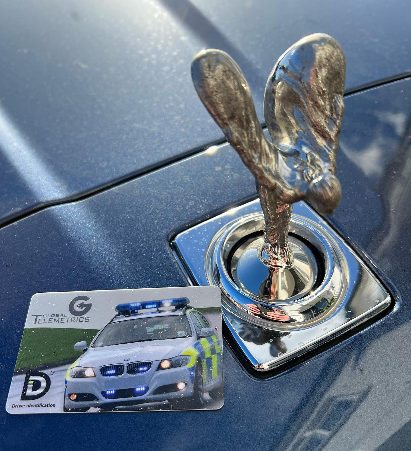 Photo of spirit of ectasy on the front of a rolls royce next to a tracker recognition card